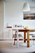 White chairs at wooden table below pendant lamps with white lampshade in bright interior
