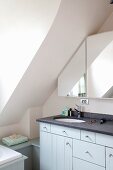 Waschtischmöbel mit Steinplatte und hellblauem Unterschrank vor massgefertigtem Spiegelschrank an Wand unter Dachschräge