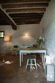 Kitchen table and wooden stools against white-painted stone wall below rustic wood-beamed ceiling