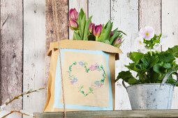 Vintage-style heart motif embroidered on paper bag and flowers on old wooden shelf