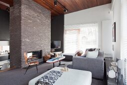 Ottoman, comfortable couch and open fireplace in free-standing brick chimney breast in open-plan interior