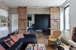 Black leather sofa combination and upholstered armchairs in living room in front of open ornate sliding elements with Moroccan doors in front of sleeping area