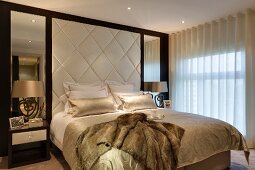 Double bed against elegant upholstered wall panel flanked by mirrors