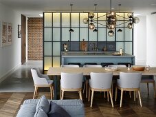 Long dining table and open-plan kitchen with counter in front of industrial-style partition wall