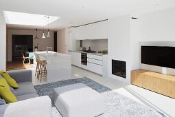 Open-plan interior with white, designer kitchen, fireplace, plasma screen, grey upholstered furniture and rug