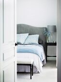 Blick durch offene Tür auf Bett mit geschwungenem, gepolstertem Kopfteil in elegantem Schlafzimmer