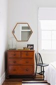 Vintage chest of drawers in front of polygonal mirror in corner of bedroom