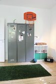 Basketball basket mounted on locker and strip of artificial grass on wooden floor