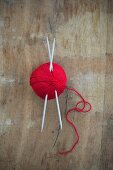 Ball of red wool with knitting needles on wooden surface (top view)