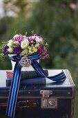 Romantic flower arrangement and antiquarian books on vintage suitcase decorated with elegant ribbon and brooch