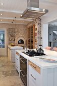 Modern, open-plan kitchen with exposed brick wall, masonry pizza oven and fitted, glass-fronted cabinet