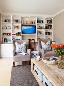 Gemütliches Wohnzimmer mit weißem Einbauregal, Fernseher und beigefarbenen Sesseln