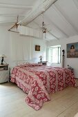 Doppelbett mit rot-weiss gemusterter Tagesdecke in Schlafzimmer mit weißer Holzdecke