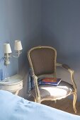 Antique, Rococo-style armchair next to console table on pastel-blue wall