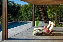 Sun loungers with pale cushions and bolsters on large wooden terrace with roof