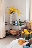 View across coffee table to vase of yellow flowers on retro serving trolley in corner of living room