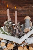 Advent arrangement of two lit candles in vintage-style preserving jars against rustic wooden wall
