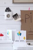 Hand-crafted birthday cards with balloon motifs below black and white photos on white wooden wall
