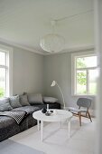 Weisser, runder Couchtisch und gemütliches Polstersofa in Wohnzimmerecke in minimalistisch, skandinavischem Flair