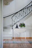 Vase of lilac and Buddha figurine on white wooden table at foot of winding staircase with delicate wrought iron balustrade in foyer