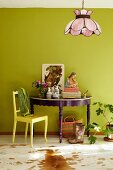 Violett lackierter, dekorierter Konsolentisch mit gelbem Holzstuhl vor hellgrüner Wand, eklektisches buntes Flair