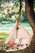 Romantic picnic in open-fronted teepee under tree in idyllic summer landscape