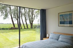 Modernes Schlafzimmer mit raumhoher Glasfront auf sonnigen Rasen