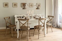 White, set dining table, wooden chairs and lit candles in vintage-style dining room