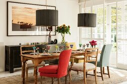 Various upholstered chairs around set wooden table below modern pendant lamps with charcoal-grey lampshades