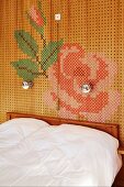 Doppelbett an Wand mit Lochholzpaneelen, darauf Blumenmuster in Stick-Optik