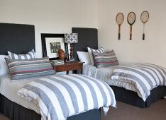 Twin beds with upholstered headboards, striped bed linen and three old tennis racquets on wall