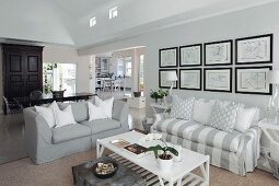 White and grey sofas below drawings on wall; dining area in background