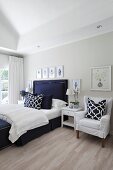 Helles Schlafzimmer mit elegantem dunkelblauem Bett, grafisch gemusterten Kissen und Bildergalerie