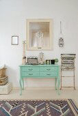 Vintage portable radio, apothecary bottles and tin on green-painted console table next to vintage folding chair leant against wall