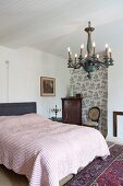 Double bed with striped bedspread, vintage-style chandelier suspended from white wooden ceiling in rustic, traditional bedroom