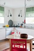 Round wooden table and red chairs in kitchen with white base units