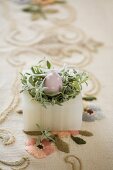 Easter nest made from china egg and green plant in alabaster pot on embroidered vintage tablecloth