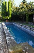 Long narrow pool with weathered stone surround in Mediterranean garden
