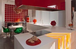 White kitchen counter, red extractor hood and dining table and chairs in front of red glass wall tiles in open-plan kitchen