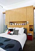 Double bed, elegant leaf-patterned bedspread and custom wooden partition at head in bedroom