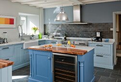 Country-house kitchen with pale blue fronts, central island with marble and walnut worksurfaces and integrated wine rack