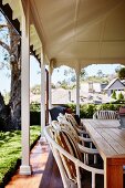 Wicker chairs at wooden table on veranda with white-painted wooden pillars