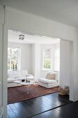 Blick durch breiten Durchgang in gemütlichen weißen Wohnraum, Polstersessel und Sofa um Coffeetable mit organischer Tischplatte