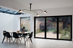 Three-armed ceiling lamp, dining table and black shell chairs in front of terrace doors