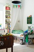 Spindly, white metal bed under canopy next to tall narrow shelving in girl's bedroom