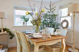 Gedeckter Tisch mit Blumenstrauss, in ländlichem Esszimmer und geschmückter Weihnachtsbaum in Ecke
