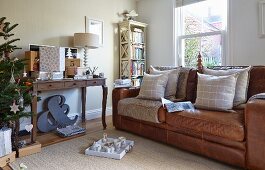 Scatter cushions on brown leather sofa below window and gifts on console table next to Christmas tree