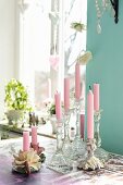 Pink candles in romantic candlesticks on table in front of window