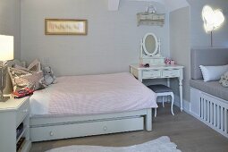 Romantic dressing table next to bed with pale pink bed linen in girl's bedroom