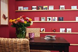 CDs on DIY shelves on claret-red wall seen across backrest of wicker chair